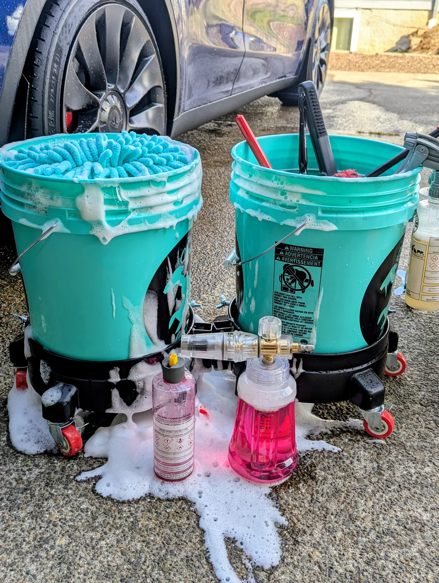 Two turquoise wash buckets, wash mitts, brushes, and detailing products beside a vehicle