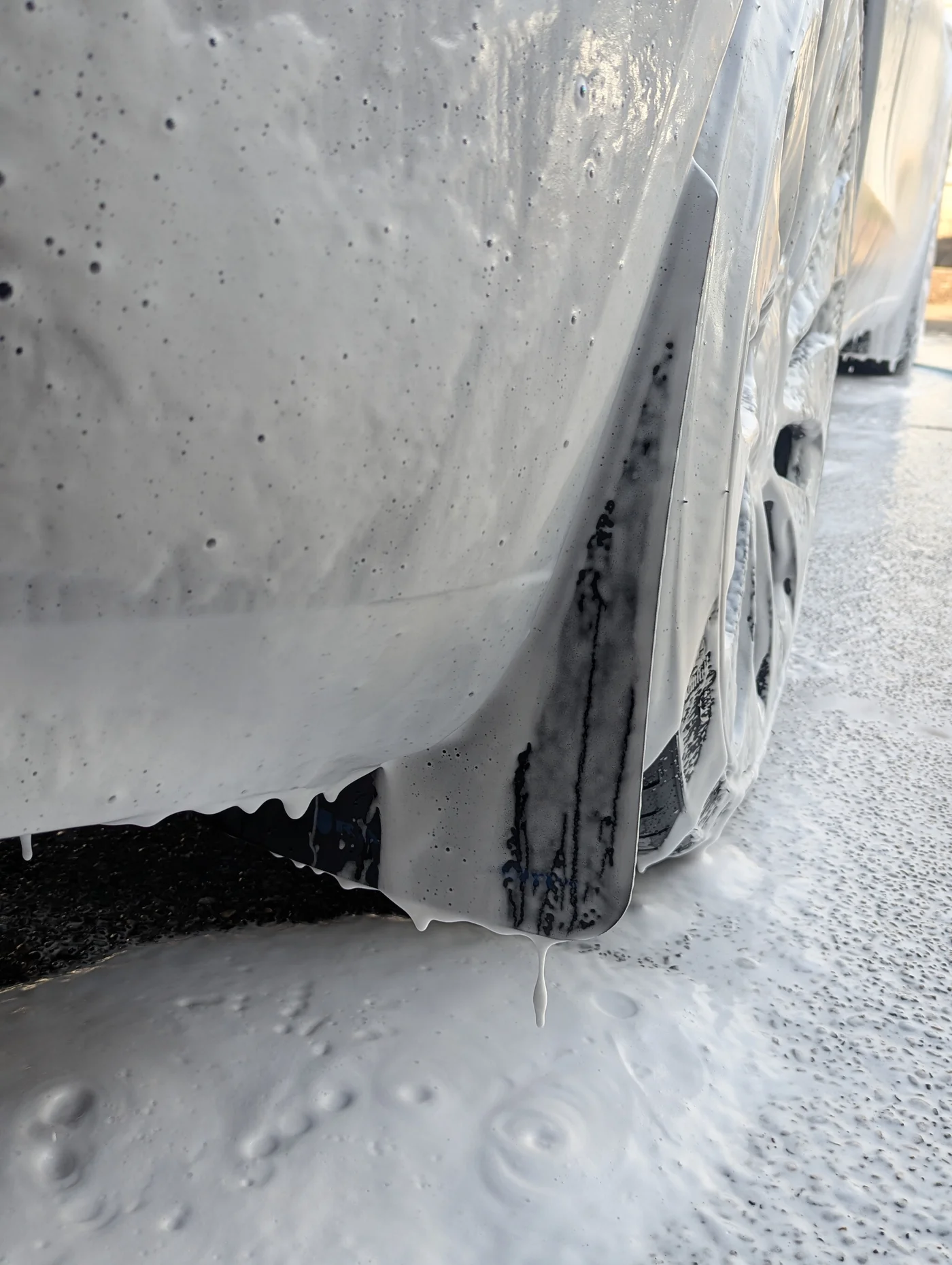Thick white soap foam covering a vehicle panel and wheel during washing